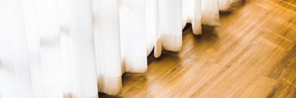 White sheer curtains along a wood floor
