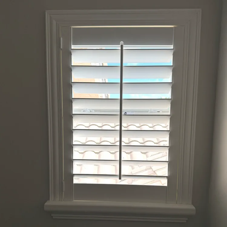 Close-up of a white plantation shutter panel with louvers tilted open to let in light